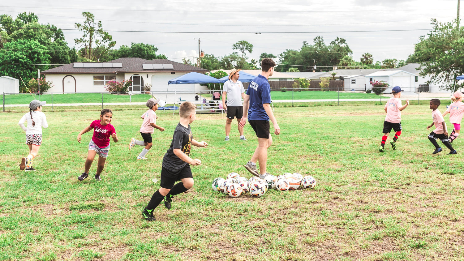 Children playing soccer on a grassy field with a cloudy sky.
